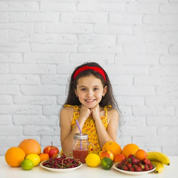 Una niña junto a una mesa con frutas.